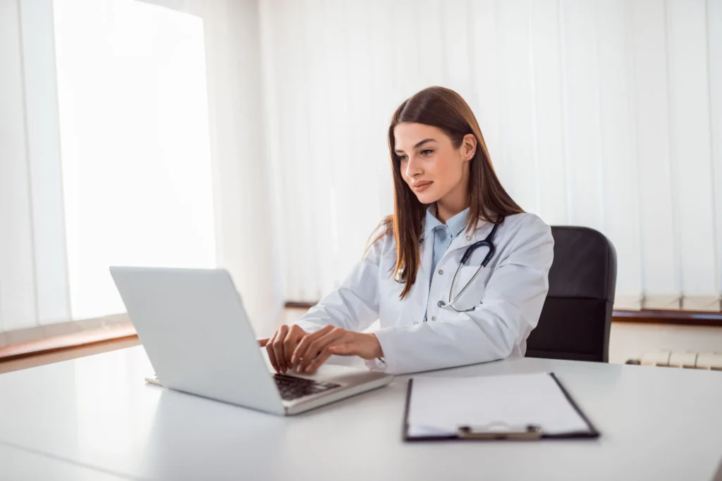 Foto de uma doutora sorrindo, utilizando o sistema de agendamento virtual da BurnUp pelo notebook da clínica de saúde onde trabalha.