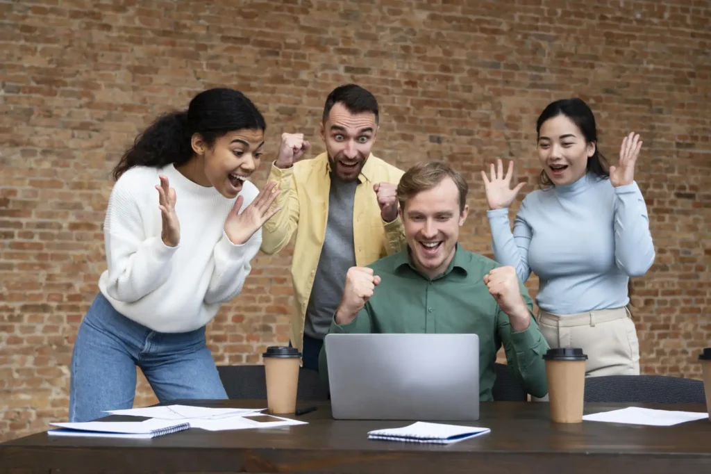 Foto de um time diverso, produtivo, motivado e engajado, que trabalha em uma empresa que promove ativamente o salário emocional, comemorando resultados positivos.