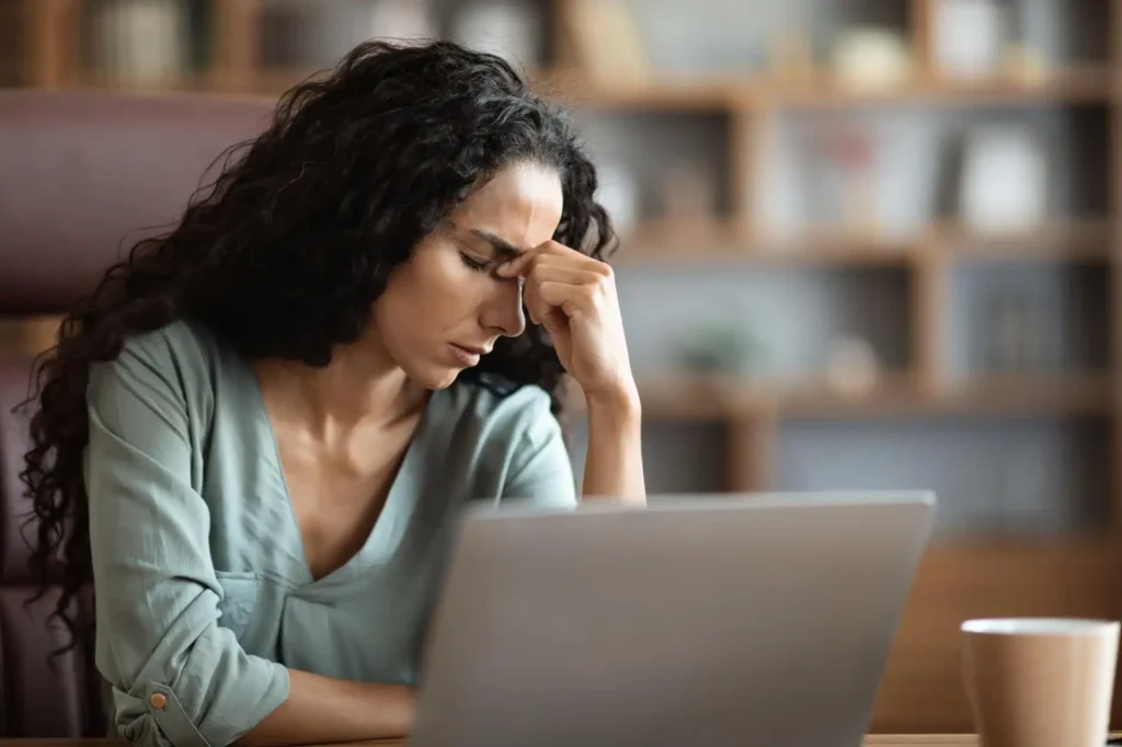 Foto de uma colaboradora cansada em frente ao laptop, com expressão de fadiga, representando os impactos da depressão no trabalho.